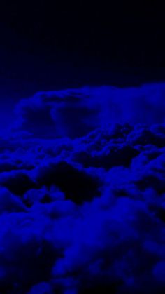 the view from an airplane looking down on clouds and blue lights in the sky at night