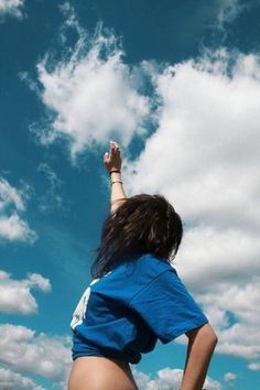 a woman flying a kite in the blue sky with white clouds behind her on a sunny day