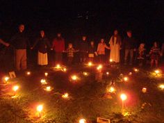 a group of people standing next to each other with candles in front of them on the ground