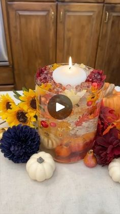 a candle that is sitting on top of a table with flowers and pumpkins around it