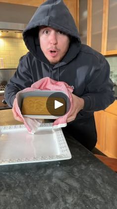 a man in a hoodie is holding a cake on a pan and making a funny face