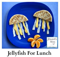 two jelly fish made out of crackers on a blue plate with orange slices and cheese