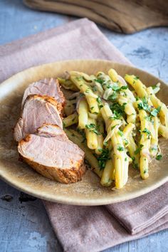 a plate with meat and pasta on it next to a fork, napkin and spoon