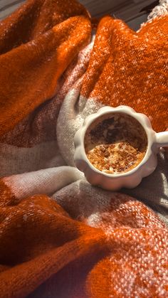 an orange and white blanket with a bowl of cereal in it sitting on top of a bed