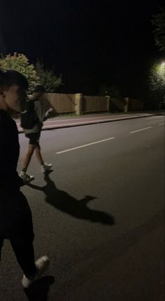 two people walking down the street at night with one person on skateboard in front of them