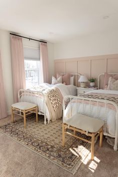 two beds in a room with pink walls and curtains on the windowsills, along with a beige rug