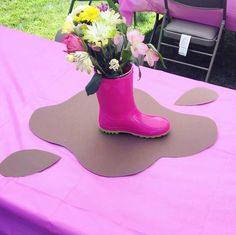 a pink boot with flowers in it sitting on a purple table cloth at an outdoor event