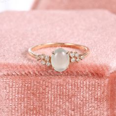 an engagement ring with a white stone surrounded by diamonds on a pink velvet cushioned surface