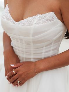 a woman in a white dress is holding her hand on her chest and wearing gold rings