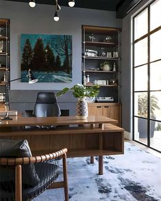 a room with a desk, chair and bookcases in front of large windows