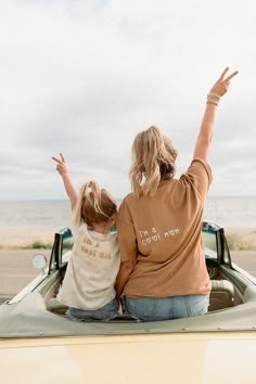 two women are sitting in the back of a car and waving to the sky with their hands up