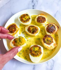 someone is pointing to deviled eggs on a white plate with mustard and parsley