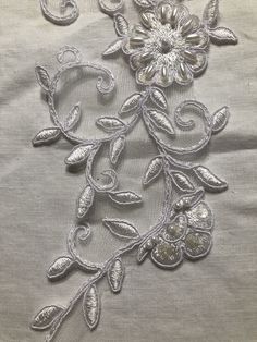 an embroidered fabric with flowers and leaves on the bottom, in white threadwork or sequins