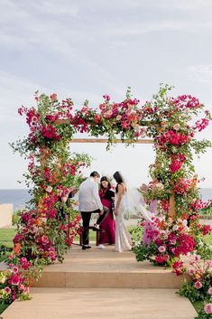 the bride and groom are getting married under an arch decorated with pink flowers on their wedding day