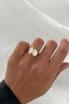 a woman's hand with a diamond ring on top of her left hand and the other hand holding an engagement ring