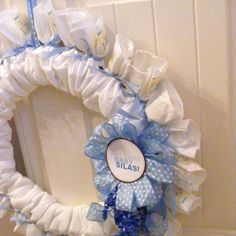 a baby shower wreath with blue and white ribbons on it's front door frame