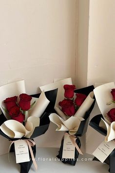 four roses are wrapped in black paper and tied with ribbons, sitting next to each other