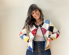 a woman standing in front of a white wall wearing a colorful jacket and denim skirt