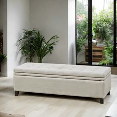 a white ottoman sitting on top of a hard wood floor next to a potted plant