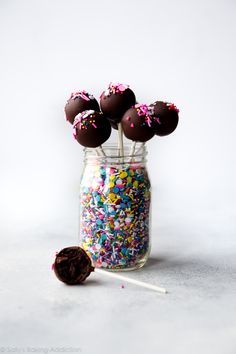 chocolate covered donuts in a jar with sprinkles and candy on a stick