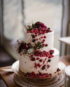 a three tiered white cake with red flowers and greenery on the top layer