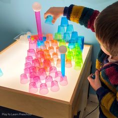 a child is playing with an illuminated table that has plastic cups and candles on it