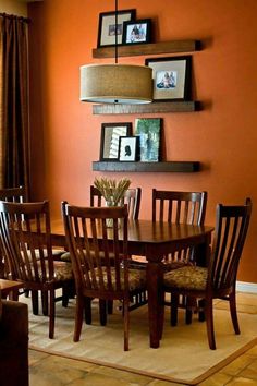 a dinning room table and chairs in front of an orange wall with pictures on it