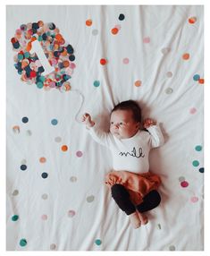 a baby laying on top of a bed with confetti and balloons in the background