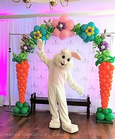 a person dressed as a bunny standing in front of some carrots and balloon decorations