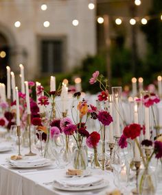 the table is set with candles, plates and flowers in glass vases on it