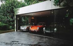 two porsches are parked in a garage with glass doors on the outside and trees behind them