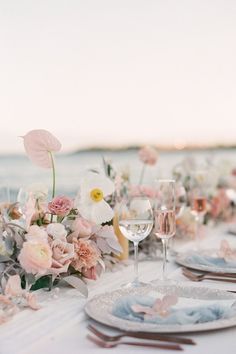 the table is set with flowers and wine glasses for an elegant wedding reception on the beach