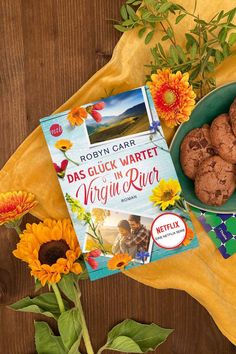 a plate of cookies next to a book and sunflowers on a yellow cloth