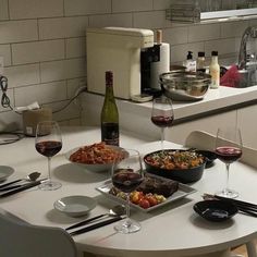 a table topped with plates and bowls filled with food next to wine glasses on top of a counter