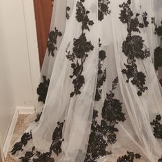 a white and black wedding dress with flowers on the skirt is hanging in front of a door