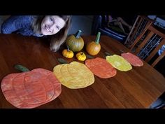 a woman sitting at a table with paper cut out of pumpkins and leaves on it