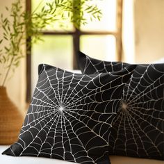 two black spiderweave pillows sitting on top of a white couch next to a plant