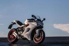 a white motorcycle parked on top of a parking lot next to a blue and cloudy sky