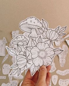 someone holding up a sticker with flowers and mushrooms on it in front of paper cutouts