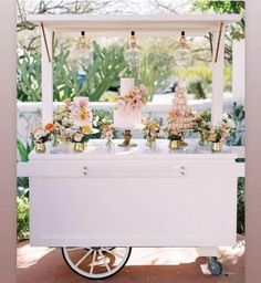 an ice cream cart is decorated with flowers and hanging lights for desserts on the table