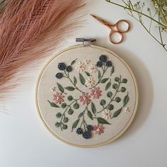 a cross stitch pattern with flowers and leaves on it next to some pink feathers, scissors and a pair of scissors