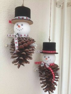 two snowmen are hanging from pine cones on the wall and one is wearing a top hat