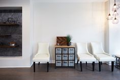 three white chairs sitting next to each other in front of a wall with shelves on it