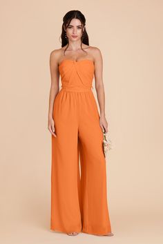 a woman wearing an orange strapless jumpsuit with high waist and wide legs, in front of a beige background