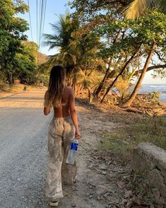 a woman walking down a dirt road holding a water bottle