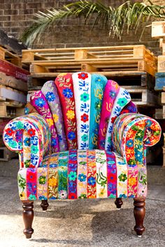 an upholstered chair with colorful fabric on it's back and arms, sitting in front of pallets