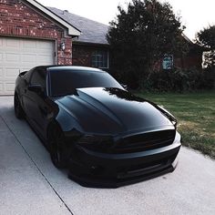 a black mustang parked in front of a house with the door ajar to show it's paint job