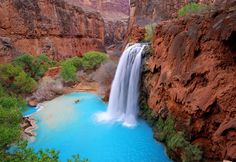 a waterfall is seen in the middle of a canyon with blue water and green trees