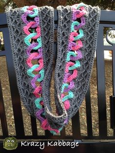 two crocheted scarfs hanging on a fence with trees in the back ground