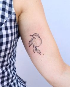 a woman's arm with a small tattoo of an orange and leaves on it